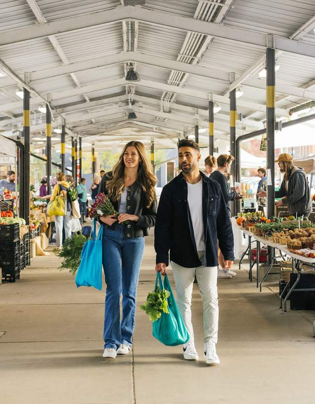 Young couple with shopping totes walking through the Ann Arbor Farmers Market