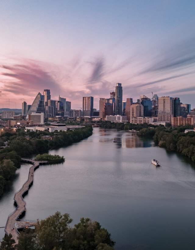 View of the Austin city skyline over Lady Bird Lake with pink and purple sky at sunset and a tour boat on the water below