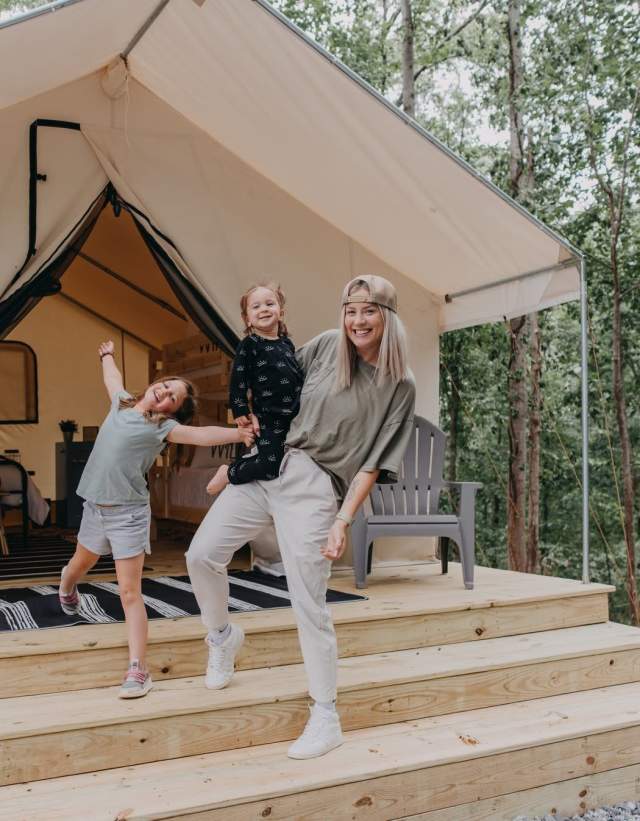 A mom and two children sit on the front porch of the Deluxe Safari tent at Timberline Glamping in Oak Mountain State Park.