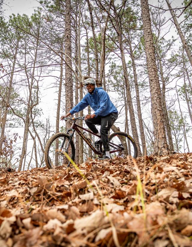 A mountain biker rides on a trail full of crunchy brown leaves.