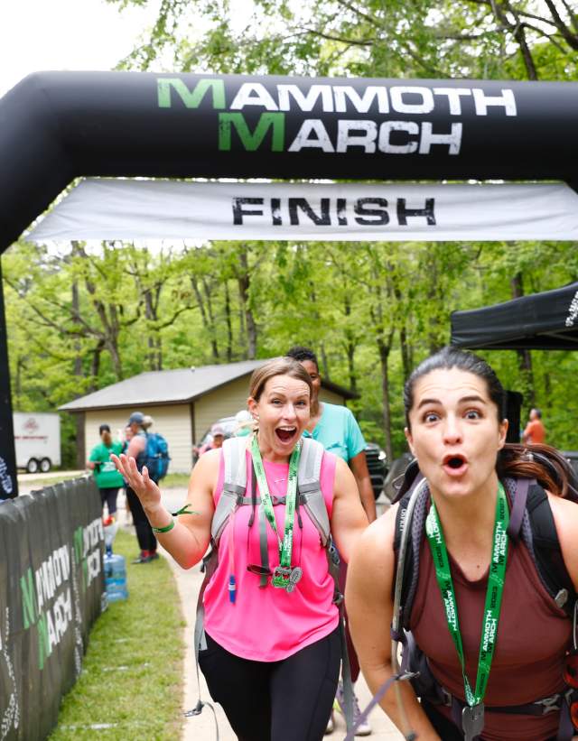 Two women walk through the finish line at MammothMarch Hiking Challenge at Oak Mountain State Park.