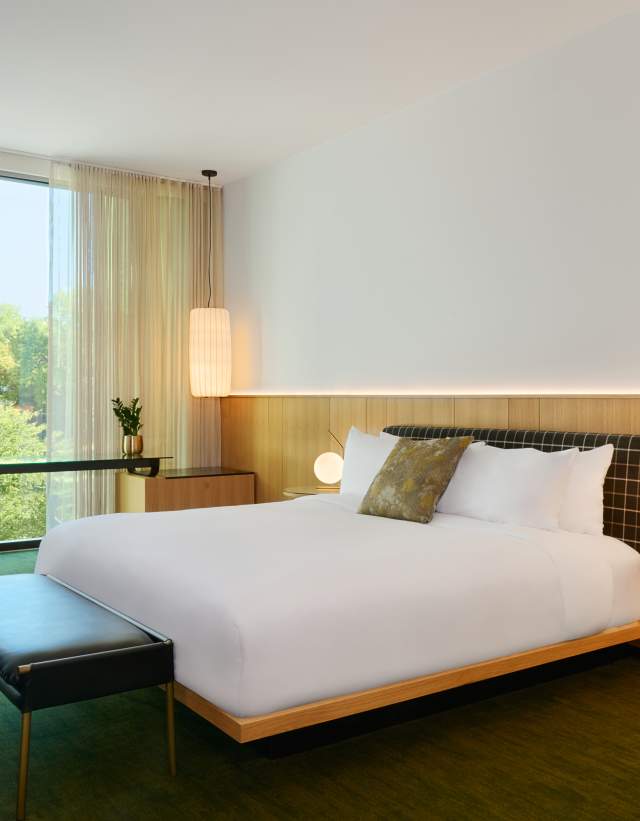 A hotel room with a bed, accent chair and large window at The Loren Hotel.