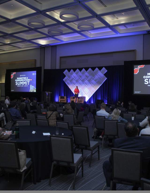 Woman standing on stage at DI Marketing & Communications Summit 2025, giving a welcome message to attendees in a ballroom.