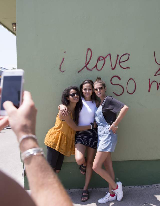 Girls posing at I Love You So Much Mural while friend takes photo