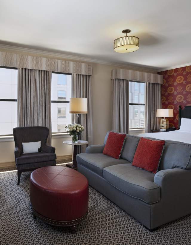Hotel room with king size bed, leather couch, sitting area and red patterned wallpaper.