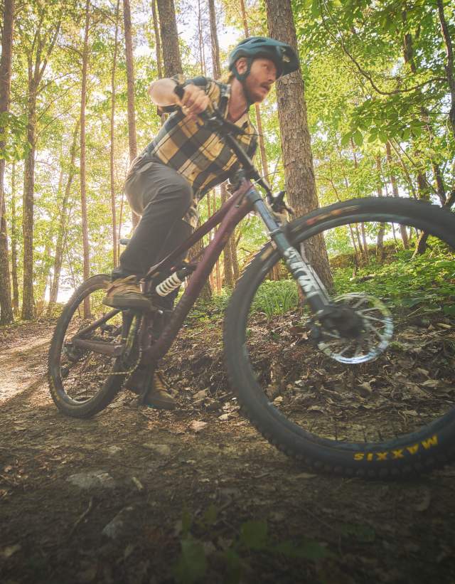 A mountain biker zooms across the trails at Double Oak Park in Shelby County. The sunlight streams through the trees behind him on the rocky trail.
