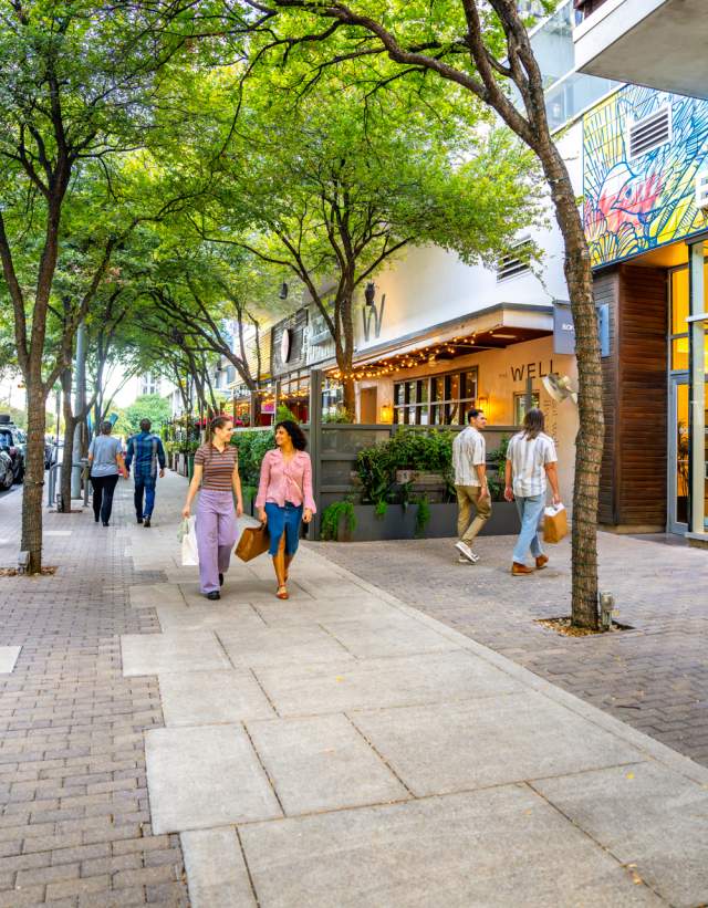 People walking on the sidewalk through the 2ND Street District chatting while holding shopping bags.