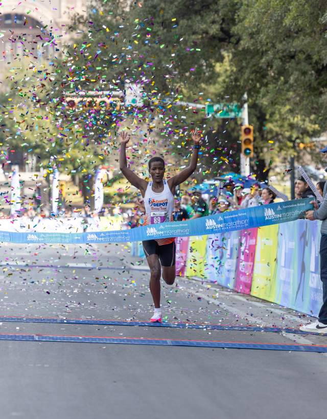 Image of a man crossing the finish line with his hands in the air at the Austin Marathon.