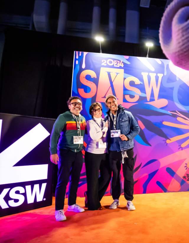 Conference attendees taking their picture in front of a SXSW mural in the registration area.