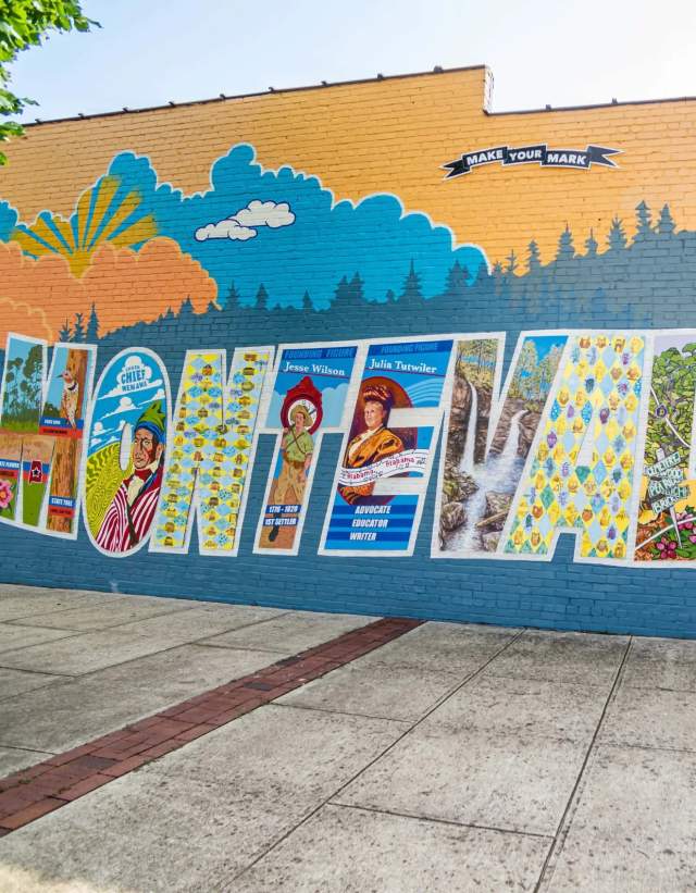 A mural in Montevallo of significant landmarks and historical stories painted into the word "Montevallo" with a sign overhead that says, "Make your mark."