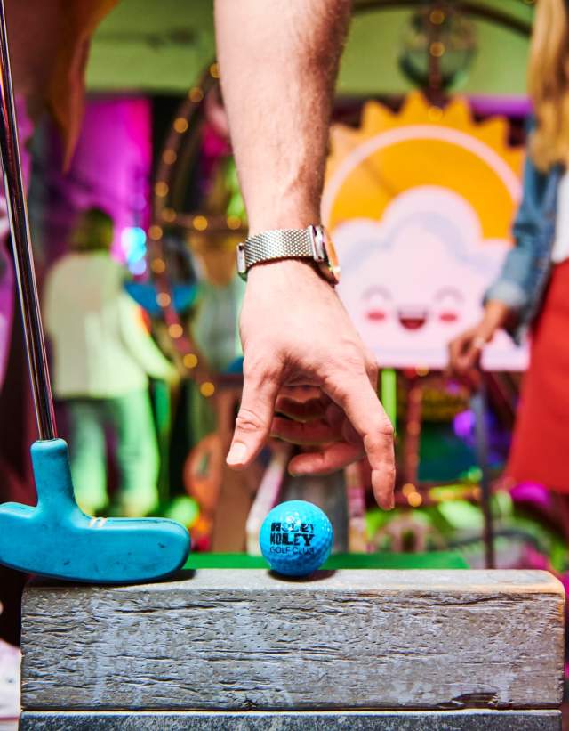 Man placing a golf ball on a raised platform in front of a colorful hole.