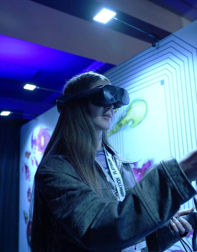 Woman using VR headset and controllers in a conference exhibit booth.