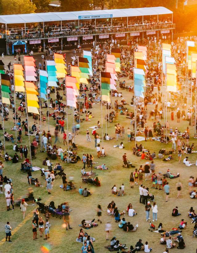 Festival goers sitting and laying around the festival grounds near food tents and festival flags.