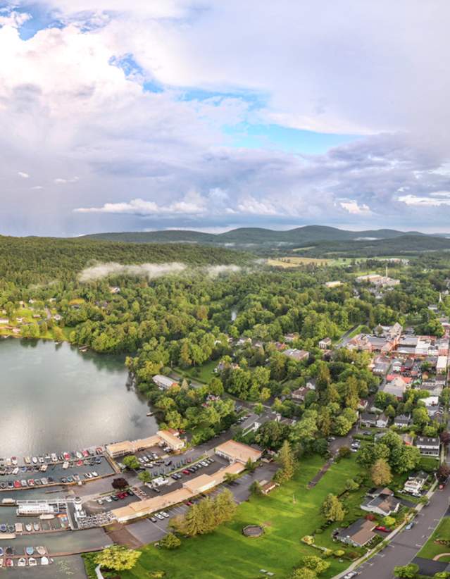 An aerial view of the Village of Cooperstown with a lake and docks to the left and village and rolling hills to the right.
