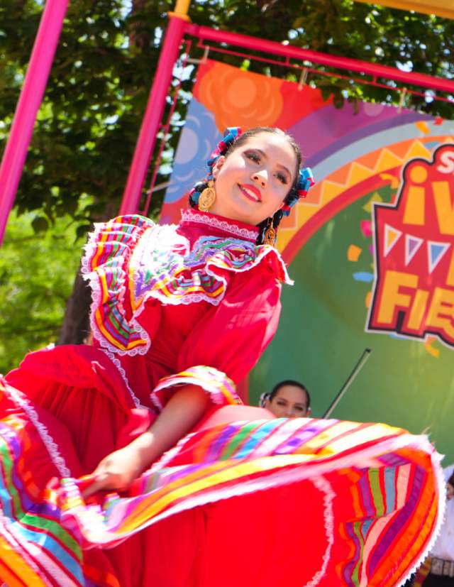 Folklorico dancer in red dress dancing with mariachi band behind her.