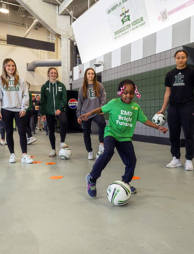 Small girl playing with soccer ball while other your girls watch on