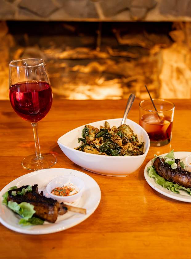 Picture of food on plates with glass of wine and mixed drink on a table by the fireplace at Penn's Tavern