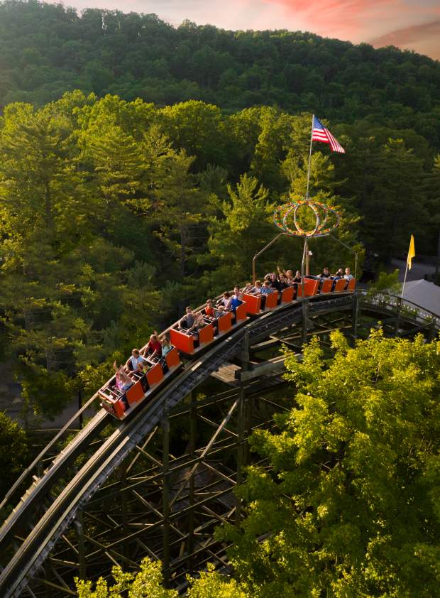 Knoebels Phoenix wooden coaster in Pennsylvania, with a train of riders descending a track through a green forest landscape.