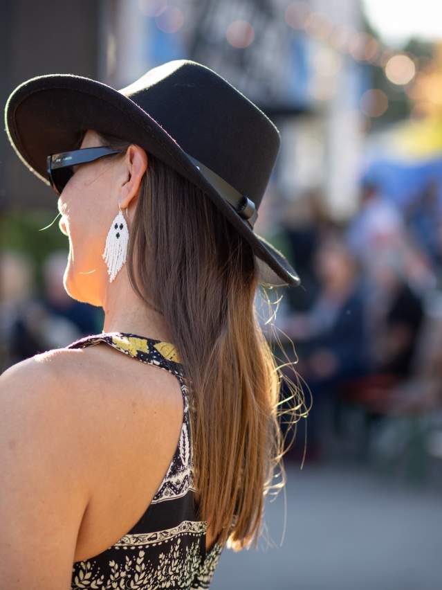 A woman in a cowboy hat and Halloween earrings holds a drink and takes pictures of live music with her phone outside at Maiden Alley Cinema's Oktoberfest.
