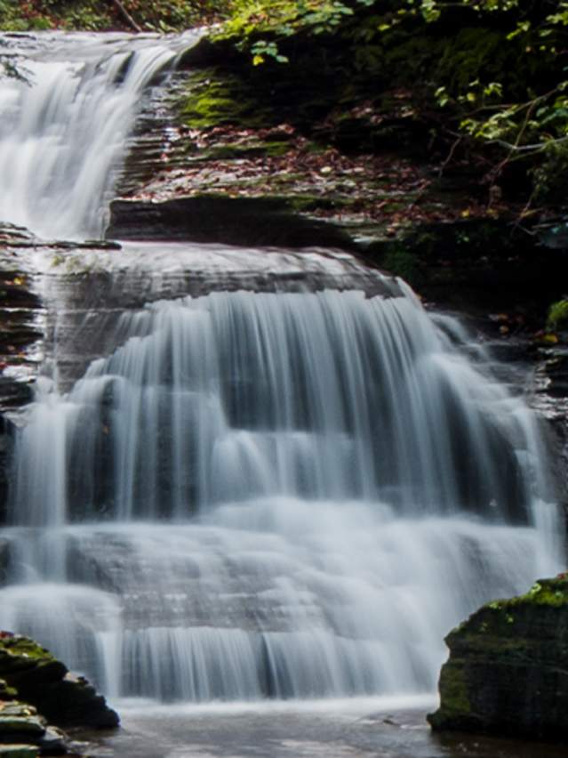 Ithaca Falls in Ithaca, NY with brown rocks and green foliage