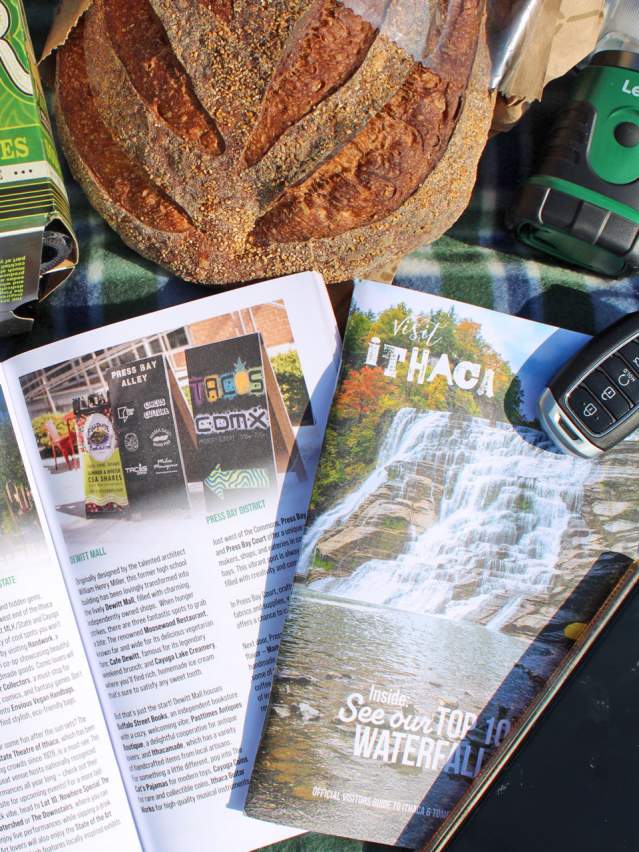 Travel guide open on picnic blanket with bread