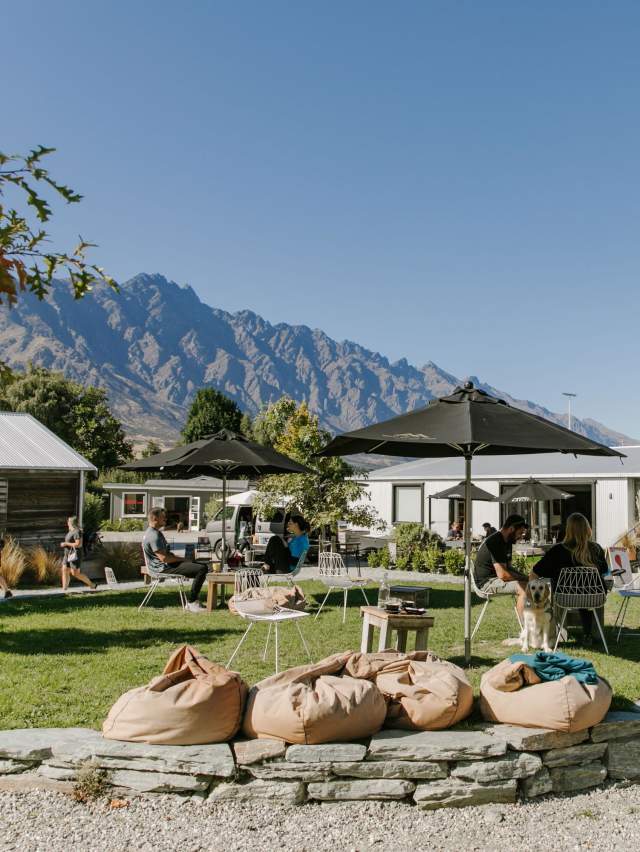 A collection of boutique shops and people sitting around a green park