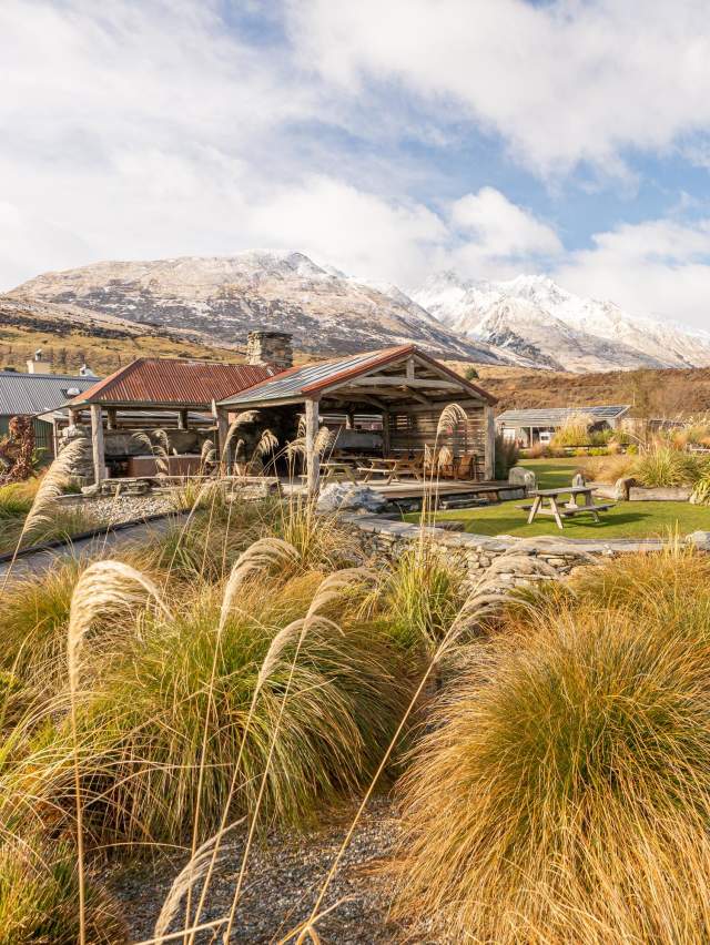 Exterior view of The Headwaters Eco Lodge, with native bush, rustic cabins and snowy mountains in the background
