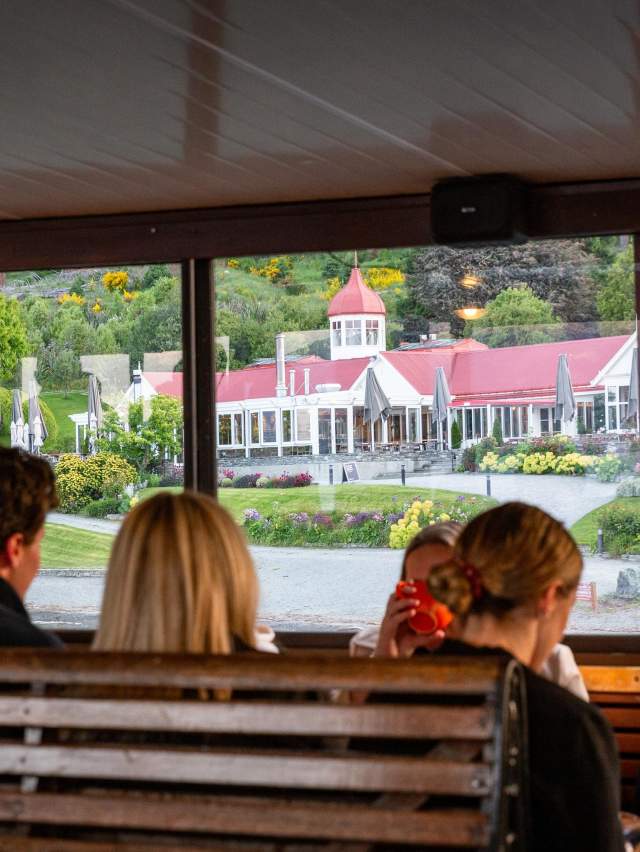 A group of people sitting on the TSS Earnslaw with a view of Walter Peak through the windows
