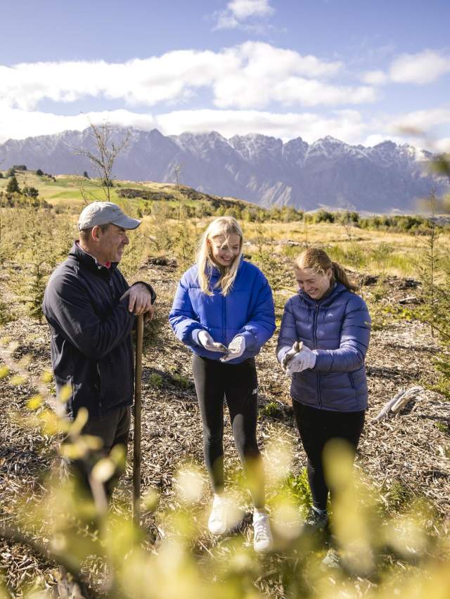 3 people working at a planting site in Queenstown, planting native trees to reforest the area with native bush