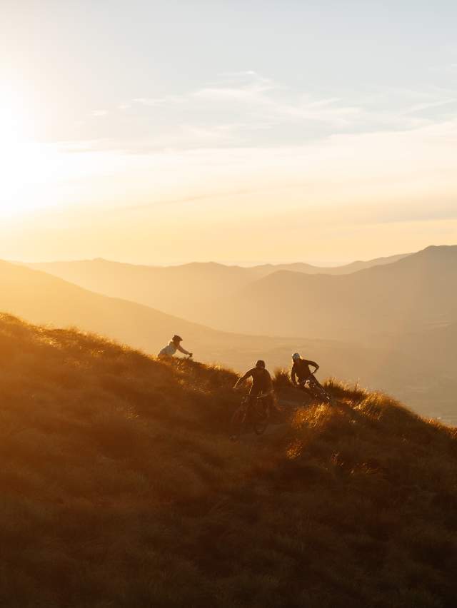 Three people biking on a mountain at sunset