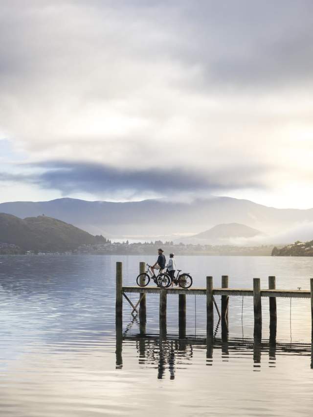 Two people at a pier with bikes overlooking a lake