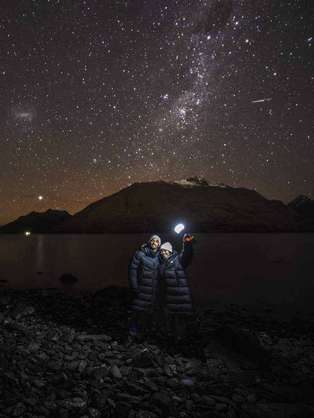 Two people holding a light with a background of mountains and a starry night sky