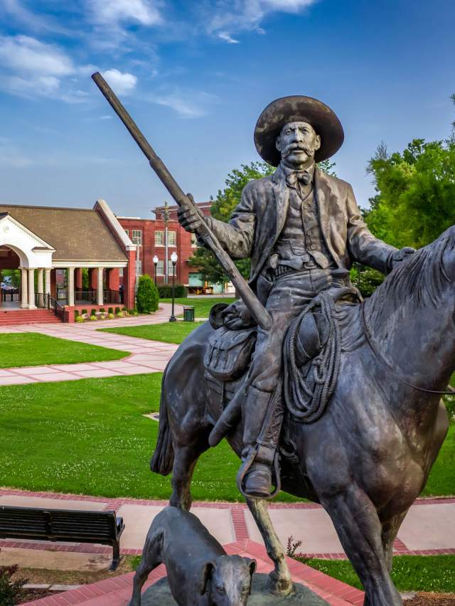 A statue portrays U.S. Marshal Bass Reeves atop a horse holding a gun with his trusty dog running next to him.