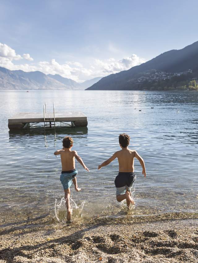 Young boys running into the water at Queenstown Bay in summer