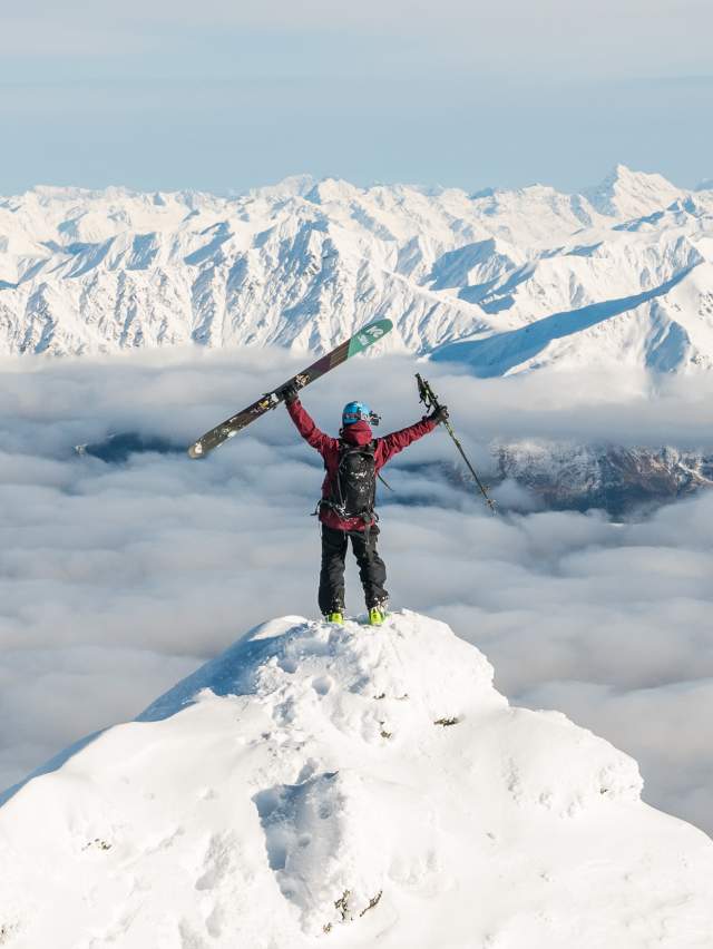 Person standing on the summit of a mountain with snowy peaks in the distance