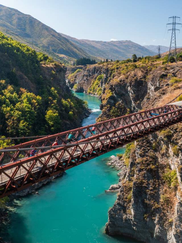 People biking over a bridge with vibrant blue water below