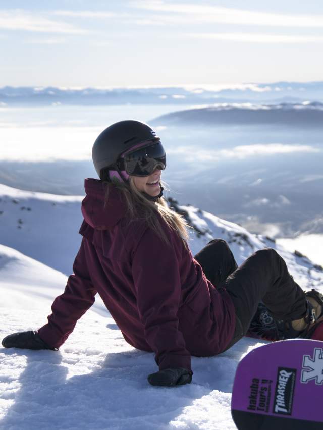 Lady snowboarder resting at the top of the mountain