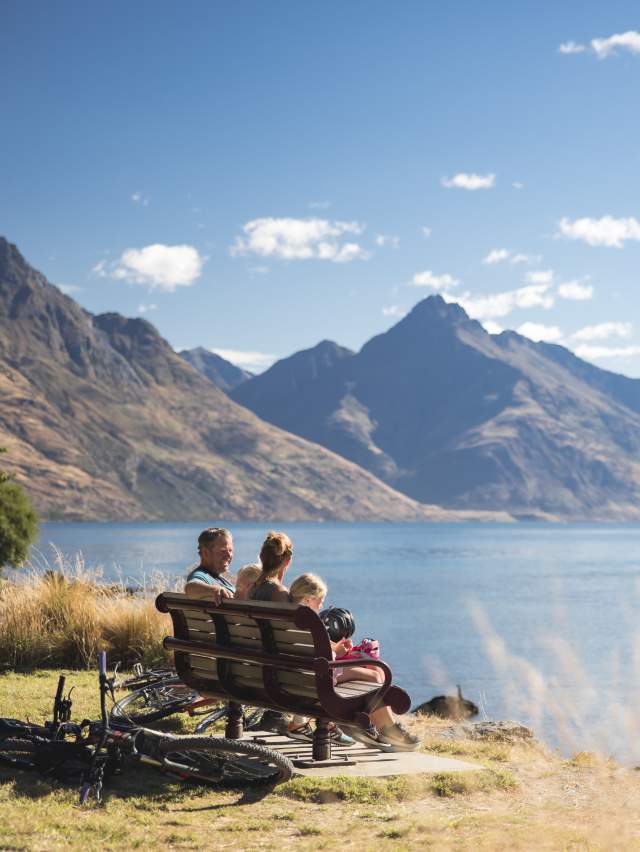 Family sitting on bench along the Queenstown Garden's Trail overlooking mountains