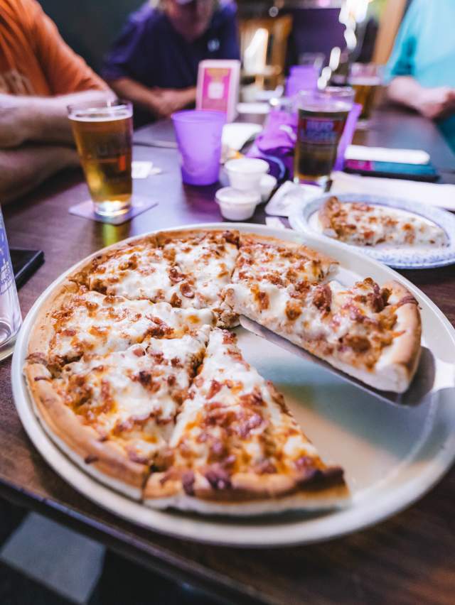 A delicious pizza sits on a table at Papas Pub, where friends are waiting to eat.