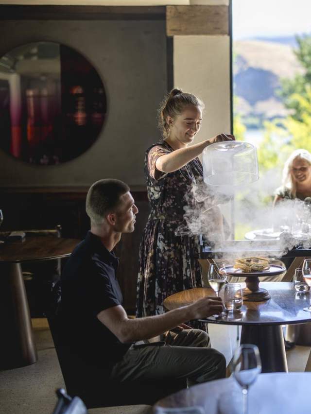 Waitress serving guests at Amisfield Restaurant, lifting up a lid of a dish with smoke coming up