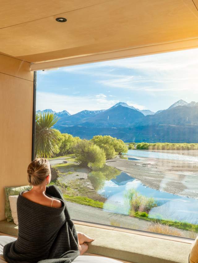 Woman looking out a huge window with view of mountains and lake at Kinloch Wilderness Retreat