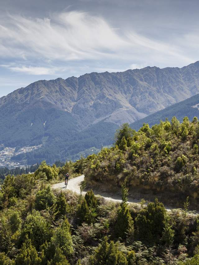 Person biking Jack's Point Trail, with Queenstown and Ben Lomond mountain in the background