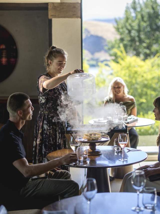 Waitress serving guests at Amisfield Restaurant, lifting up a lid of a dish with smoke coming up