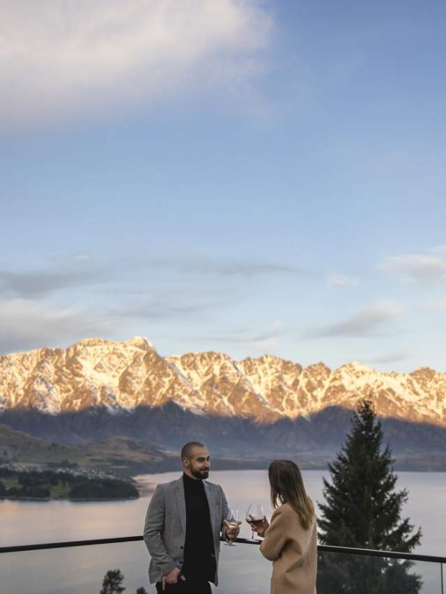 People enoying a wine on the balcony of Nest Kitchen and Bar overlooking the snow-covered Remarkables mountain range