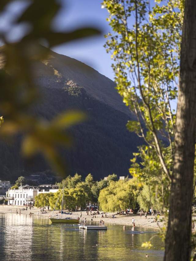 Looking through green trees to big lake, boats, people and buildings