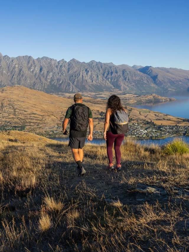 Two people walking with the Remarkables mountain range in the background