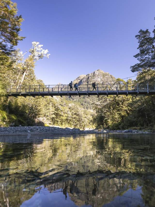 Ground of friends crossing a swing bridge on the Routeburn Track with a mountain in the background