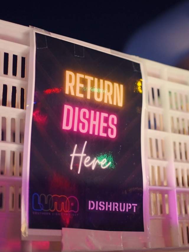 Sign illuminated by different coloured lights that read Return DIshes Here, LUMA x DISHRUPT