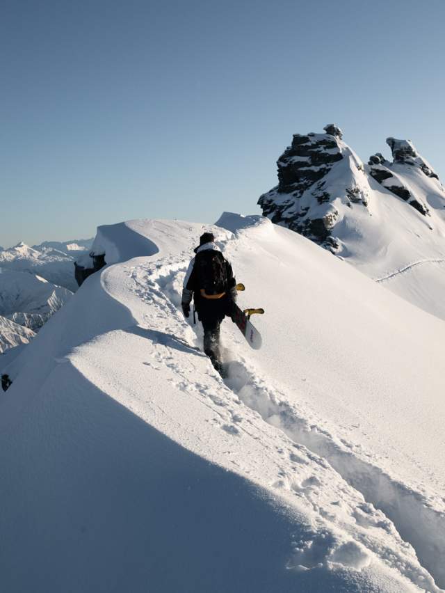 Snowboarder hiking to Treble Cone summit in powder