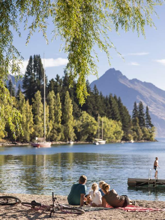 Family and bikes on the beach in Queenstown in summer, boys playing on the pontoon.